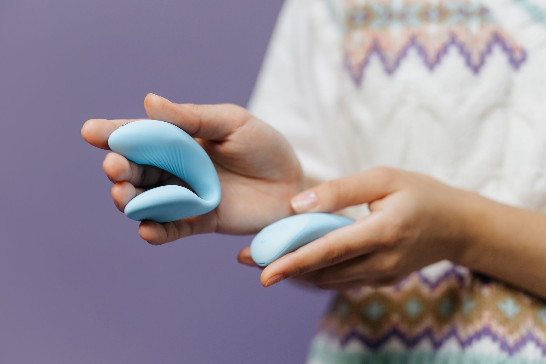 Hand holding a personal vibrator against a purple background