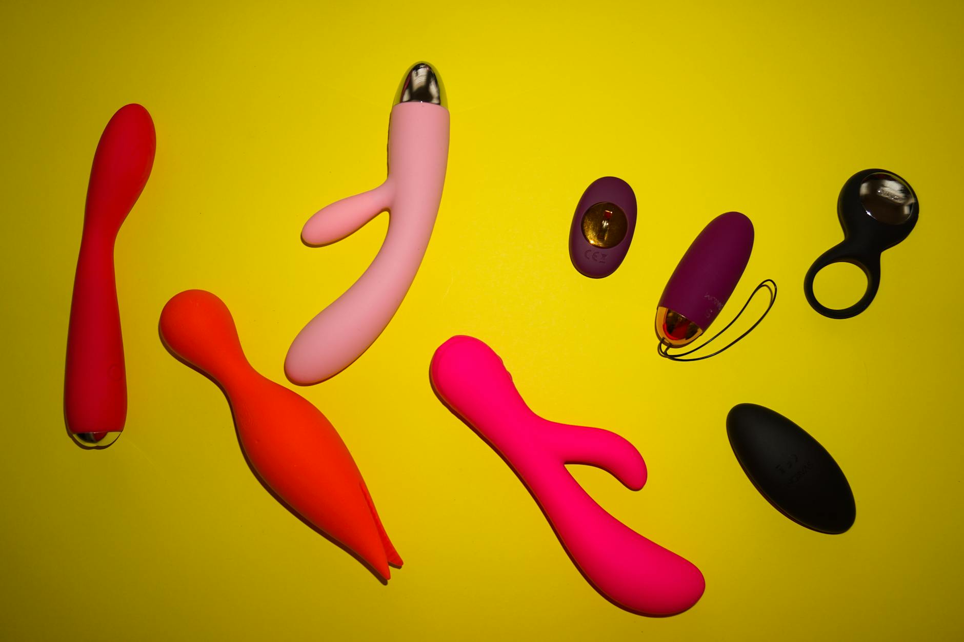 Colorful sex toys arranged on a bright yellow surface, showcasing vibrator designs and variety